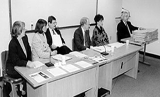 Judge Joseph Lauria (far right), the Chief Administrative Judge for the New York City Family Courts, points to the stack of 100 files that represent the average caseload of one assigned counsel.