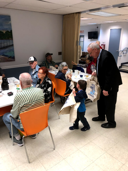 Assemblyman Jeffrey Dinowitz is helped by his grandson as they distribute reusable canvas bags from Citizens Committee of New York City to seniors at Riverdale Senior Services.